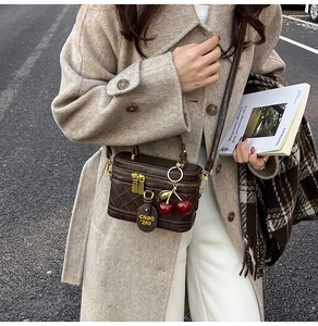 Close-up of brown quilted box bag with gold zippers and a red cherry charm on a coat