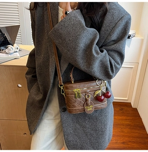 Detail of a brown quilted box bag with cherry charm and adjustable leather strap