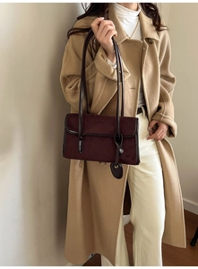 Detail of dark burgundy suede underarm bag with slim straps and round charm on wool coat