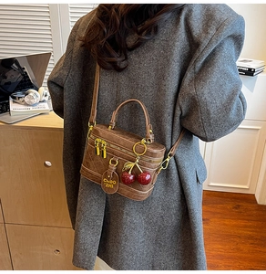 Brown quilted box bag with cherry charm shown on model in a modern office setting