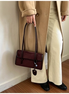 Detail of burgundy suede shoulder bag with twin straps and circular pendant on model