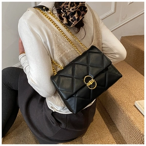Close-up of black quilted shoulder bag with gold chain straps and a metallic twist lock