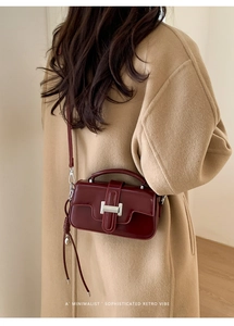 Deep red rectangular leather handbag with silver lock shown on a camel wool coat