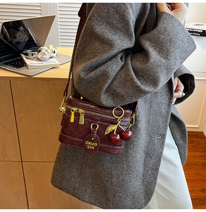 Detail of vintage burgundy quilted crossbody bucket bag with cherry charm and gold zippers