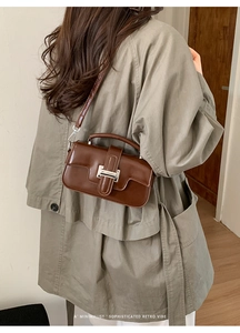 Detail of dark brown retro leather handbag worn on olive coat with silver clasp buckle
