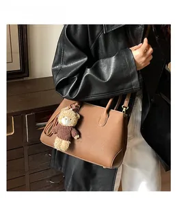 Borsa tote marrone con texture litchi e ciondolo a orsetto indossata da una modella