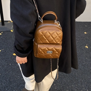 Detailed view of brown quilted backpack featuring a metallic twist lock and chain strap