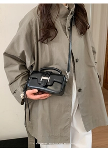 Detail of minimalist black leather crossbody bag with silver buckle on trench coat outfit