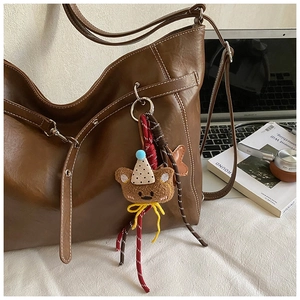 Détail d'un grand sac cabas marron avec un joli pendentif ours sur un bureau blanc