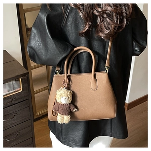 Borsa a mano marrone in pelle con ciondolo a orsetto in un ambiente lifestyle accogliente