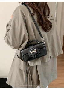 Side view of a vintage black glossy handbag with silver buckle and thin strap on a model