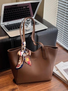 Brown leather tote bag with silk scarf decoration and laptop on a chair background