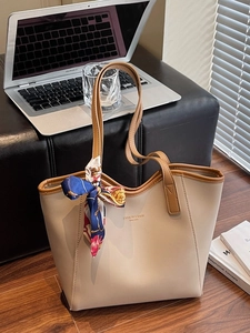 Minimalist cream leather tote bag with brown trim and silk scarf on black sofa