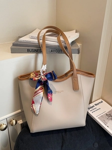 Minimalist beige tote bag with brown straps and floral scarf in a cozy indoor setting