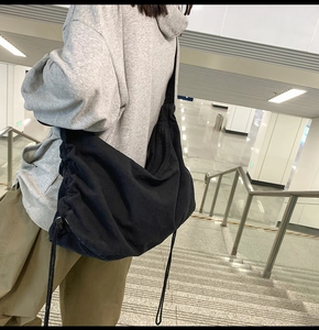 Detail of a black canvas crossbody bag featuring a unique drawstring side design and strap