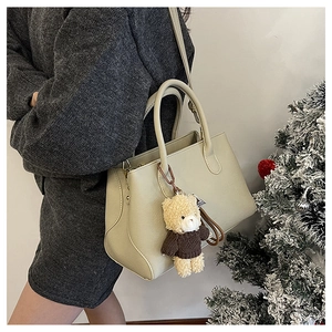 Dettaglio borsa a mano in pelle beige con ciondolo a orsetto e tracolla sottile