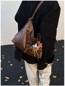 Detail of a brown leather hobo bag with white stitching and bear charm on a model