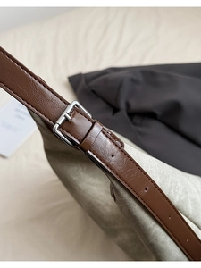 Detail of gray-green canvas tote with brown leather strap and silver buckle adjustment