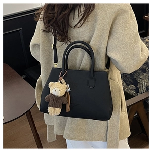 Dettaglio della borsa in pelle opaca nera con ciondolo a forma di orsetto e cappotto