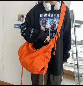 Detail of a bright orange canvas messenger bag with adjustable strap and drawstring design