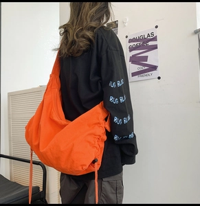 Detail of bright orange canvas crossbody bag featuring functional drawstring closure and wide strap