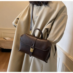 Detail der Vintage Umhängetasche in Dunkelbraun mit Goldschließe am beigen Trenchcoat