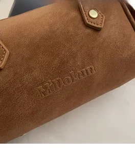 Close-up of brown Boston bag showing textured lychee leather and embossed Midolun logo