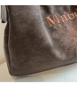 Detail of floral embroidery and retro letter pattern on dark brown leather tote bag