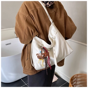 Détail d'un grand sac cabas blanc en similicuir avec breloque ours porté à l'épaule