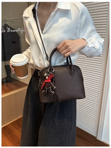 Close-up of brown lychee leather shell bag with cute bear charm and adjustable strap