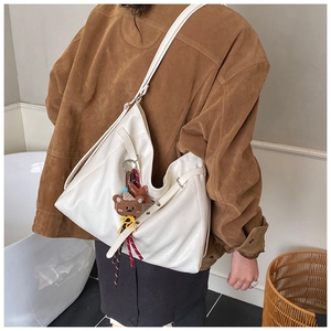 Gros plan d'un sac hobo en cuir blanc avec charm d'ours et ruban décoratif élégant