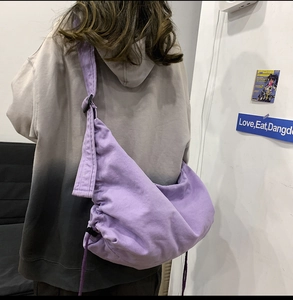 Purple canvas crossbody bag with adjustable strap and drawstring closure worn by model
