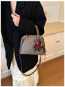 Detail of taupe shell bag with litchi texture and a cute bear charm on model