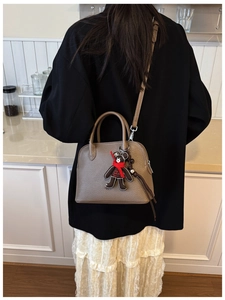 Close-up of brown litchi leather bag with cute teddy bear charm and gold zipper details