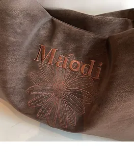 Macro detail of dark brown leather tote with Maodi lettering and floral embroidery