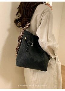 Detail of black suede tote bag with decorative silk scarf and golden buckle accents