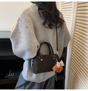 Brown mini Boston bag with plush bear charm worn by a model in a minimal room