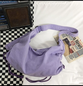 Close-up of purple canvas crescent bag with drawstring detail and thick shoulder strap