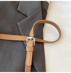 Détail de bandoulière en cuir caramel avec coutures fines et boucle argentée de sac