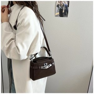 Detail view of a dark brown leather handbag with silver lock on an elegant trench coat