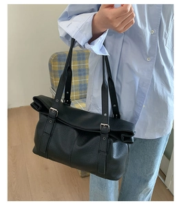 Detail of large black pebbled leather tote bag with silver buckle and vertical trim