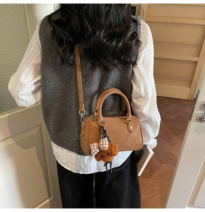 Detailed view of brown leather Boston bag with plush teddy bear charm and strap
