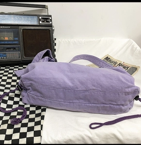 Detail view of purple canvas shoulder bag with unique side drawstring closure and retro strap
