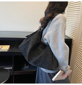 Detail of embossed logo on large black faux suede shoulder bag for daily commuting