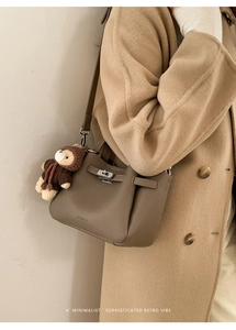 Détail d'un sac seau en cuir grainé avec breloque ours sur un manteau beige chic