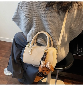 Detail of cream Boston bag with embossed logo, plush dog charm and slim shoulder strap