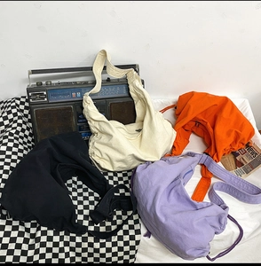 Detail of canvas crescent bags in black, cream, orange, and purple with wide straps