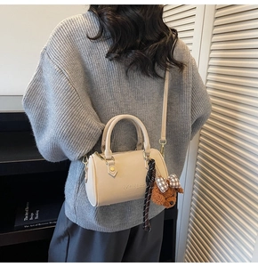 Detail of beige Boston bag featuring a plush bear charm and side leather strap detail