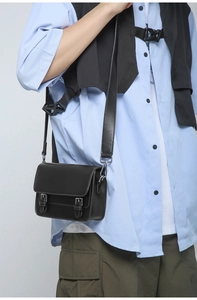 Detail of black leather crossbody bag with silver buckles and adjustable shoulder strap
