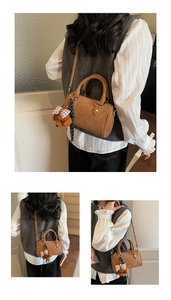 Detail view of a brown Boston handbag with embossed logo and a cute teddy bear charm